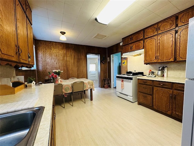 kitchen with white appliances, under cabinet range hood, a sink, light countertops, and wooden walls