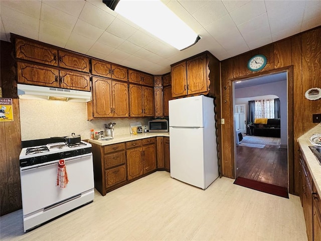 kitchen featuring white appliances, under cabinet range hood, light wood-style floors, brown cabinets, and light countertops