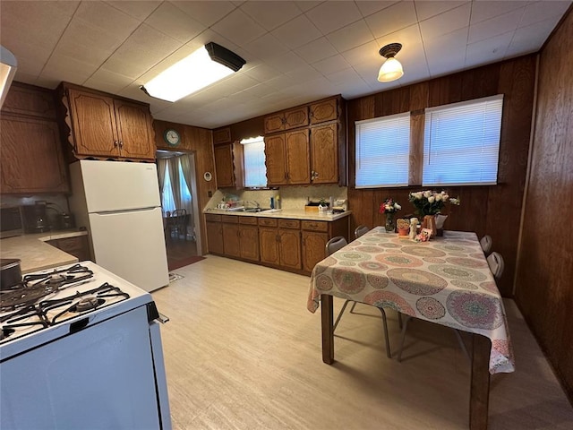 kitchen with gas range oven, freestanding refrigerator, light countertops, wooden walls, and decorative backsplash