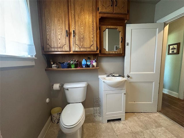 half bath with toilet, baseboards, and vanity