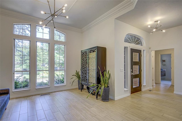 entryway with a chandelier, baseboards, ornamental molding, a towering ceiling, and light wood-style floors
