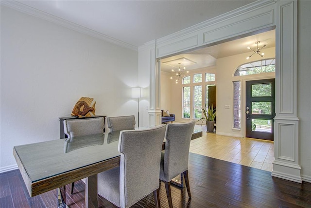 dining area featuring a chandelier, wood finished floors, baseboards, ornamental molding, and ornate columns