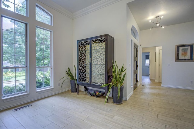 hallway featuring a towering ceiling, baseboards, light wood-type flooring, and crown molding