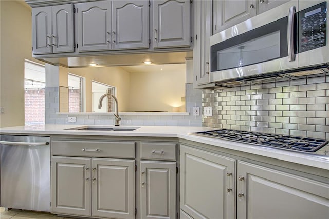 kitchen with appliances with stainless steel finishes, a sink, gray cabinetry, and decorative backsplash