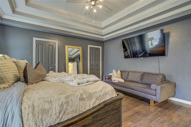 bedroom with a tray ceiling, dark wood-style flooring, baseboards, crown molding, and a textured wall