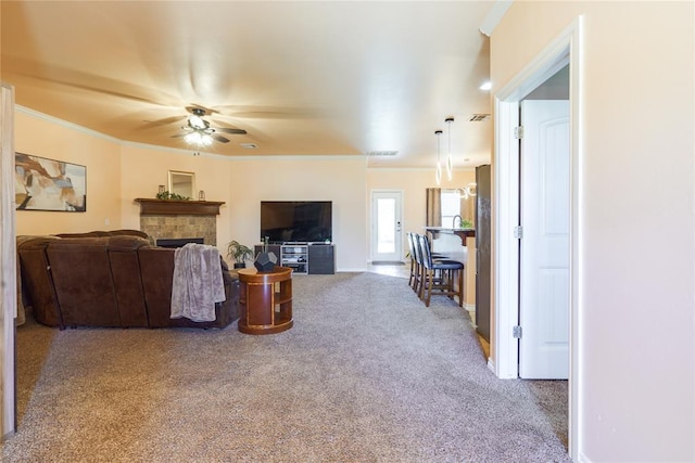 living room featuring carpet floors, a ceiling fan, crown molding, a fireplace, and baseboards
