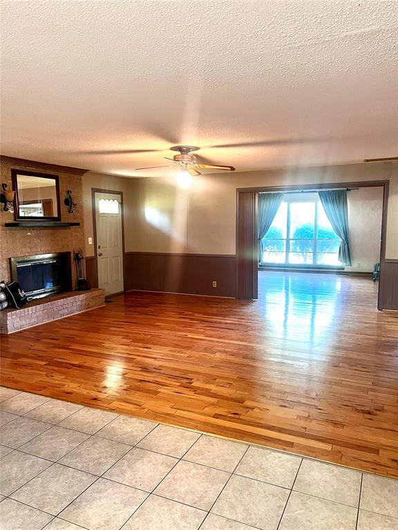 unfurnished living room with light wood-style floors, ceiling fan, a fireplace, a textured ceiling, and a wainscoted wall