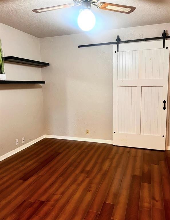 empty room with a ceiling fan, a barn door, wood finished floors, baseboards, and a textured ceiling