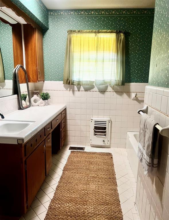 bathroom with wallpapered walls, heating unit, wainscoting, tile patterned flooring, and vanity