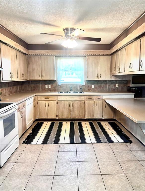 kitchen featuring white appliances, a sink, a textured ceiling, light countertops, and light brown cabinetry