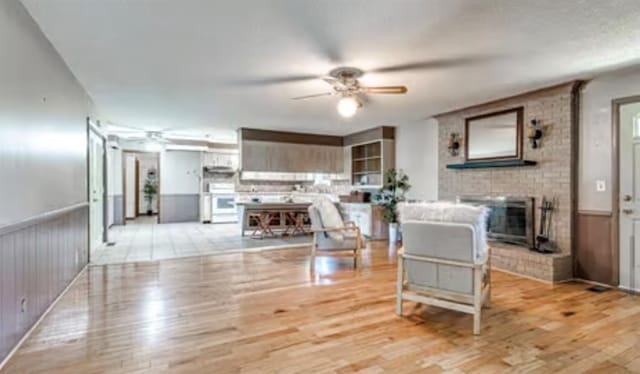 18906 13th St, Shawnee, OK 74801 - living area featuring a ceiling fan, a brick fireplace, light wood-style flooring, and a wainscoted wall