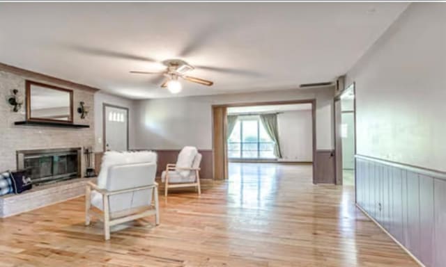 18906 13th St, Shawnee, OK 74801 - living room with ceiling fan, a fireplace, light wood finished floors, and a wainscoted wall