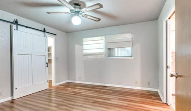 18906 13th St, Shawnee, OK 74801 - unfurnished bedroom with a barn door, wood finished floors, multiple windows, and baseboards