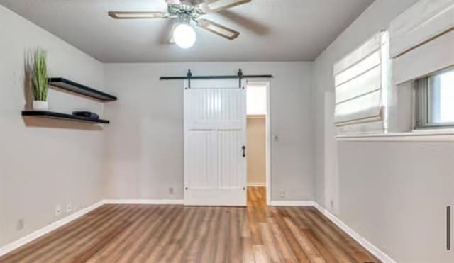 18906 13th St, Shawnee, OK 74801 - unfurnished room with a ceiling fan, wood finished floors, a barn door, and baseboards