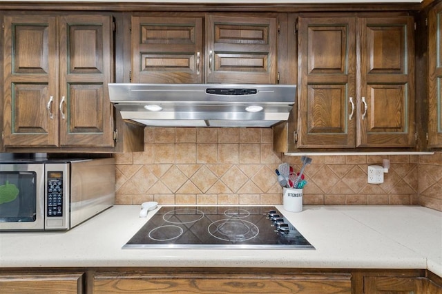 805 John F Kroutil Dr, Yukon, OK 73099 - kitchen featuring black electric stovetop, stainless steel microwave, exhaust hood, light countertops, and decorative backsplash