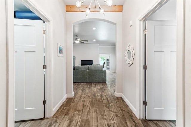 hallway with arched walkways, wood finished floors, a chandelier, and baseboards
