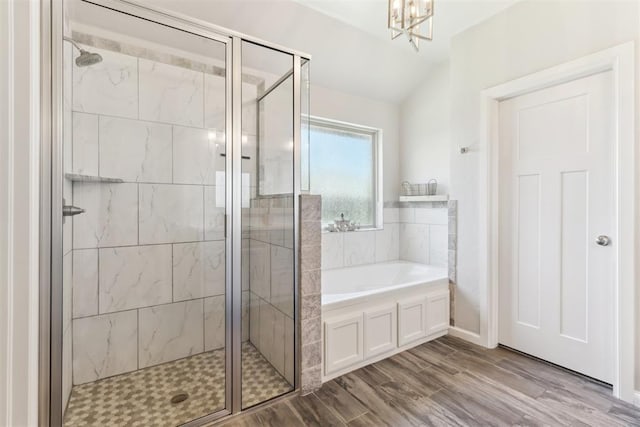 bathroom featuring a stall shower, a garden tub, a chandelier, wood finished floors, and lofted ceiling