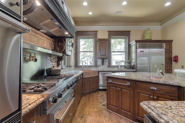 1415 N Hudson Ave, Oklahoma City, OK 73103 - kitchen with appliances with stainless steel finishes, light wood-style floors, wall chimney exhaust hood, crown molding, and light stone counters