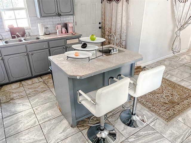 209 SW 40th St, Oklahoma City, OK 73109 - kitchen featuring gray cabinets, light countertops, a center island with sink, and decorative backsplash