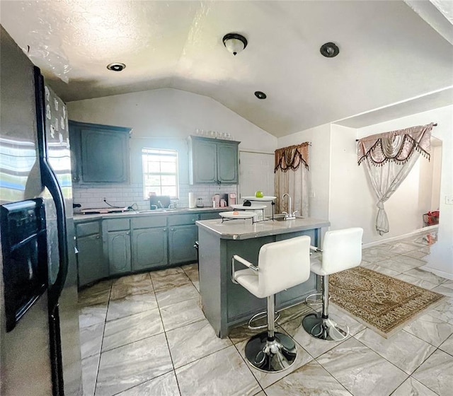 209 SW 40th St, Oklahoma City, OK 73109 - kitchen with black fridge, vaulted ceiling, decorative backsplash, light countertops, and light marble finish floors