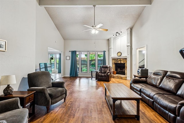 living room featuring ceiling fan, high vaulted ceiling, wood finished floors, a stone fireplace, and a textured ceiling