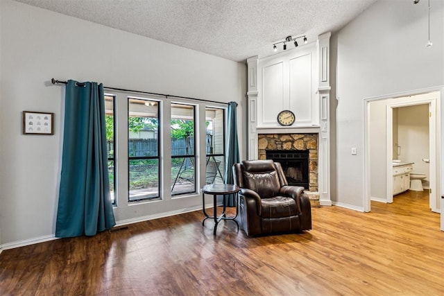 sitting room featuring a textured ceiling, light wood-style flooring, a fireplace, baseboards, and rail lighting