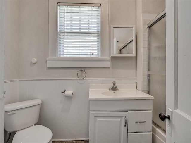 full bath with toilet, vanity, a shower with shower door, and a wainscoted wall