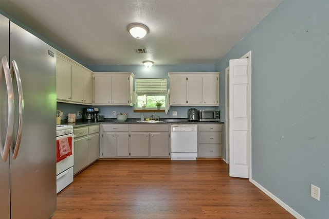 109 E Hayes St, Norman, OK 73069 - kitchen featuring appliances with stainless steel finishes, a sink, dark countertops, wood finished floors, and white cabinetry