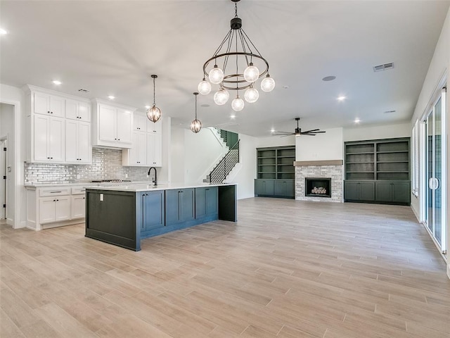 4405 Las Colinas Ln, Norman, OK 73072 - kitchen featuring a ceiling fan, white cabinets, light countertops, a stone fireplace, and a center island with sink