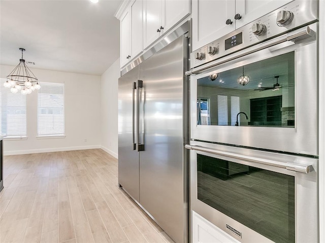 4405 Las Colinas Ln, Norman, OK 73072 - kitchen with appliances with stainless steel finishes, white cabinets, baseboards, hanging light fixtures, and light wood-type flooring