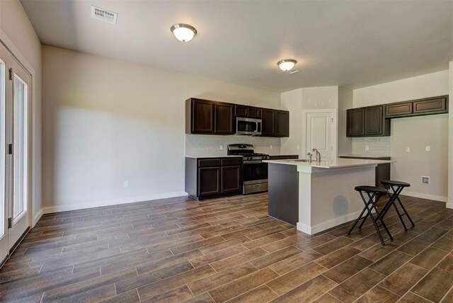 9749 Livingston Rd, Edmond, OK 73025 - kitchen with appliances with stainless steel finishes, dark wood-style flooring, light countertops, a center island with sink, and dark brown cabinets