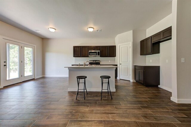 9749 Livingston Rd, Edmond, OK 73025 - kitchen featuring stainless steel microwave, wood tiled floors, stove, dark brown cabinetry, and a kitchen island with sink