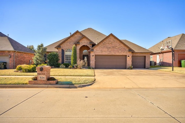924 Regal Rd, Yukon, OK 73099 - view of front of house with brick siding, a garage, driveway, cooling unit, and roof with shingles