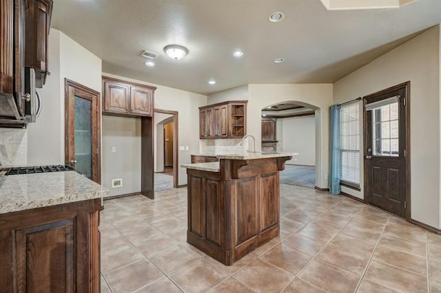 924 Regal Rd, Yukon, OK 73099 - kitchen with open shelves, arched walkways, a peninsula, recessed lighting, and light stone counters