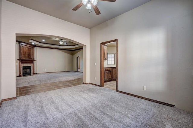 924 Regal Rd, Yukon, OK 73099 - unfurnished living room with a ceiling fan, arched walkways, light colored carpet, baseboards, and a fireplace