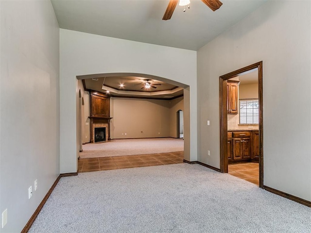 924 Regal Rd, Yukon, OK 73099 - unfurnished living room featuring ceiling fan, arched walkways, light carpet, a tray ceiling, and baseboards