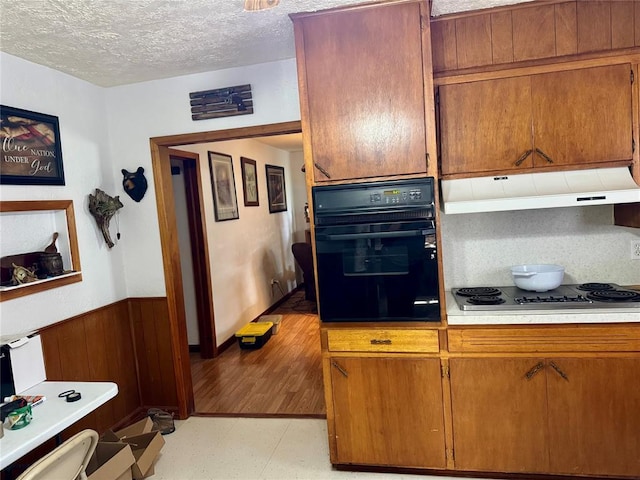 321 E Ninth St, Leedey, OK 73654 - kitchen featuring black oven, under cabinet range hood, light flooring, stainless steel electric stovetop, and a textured ceiling