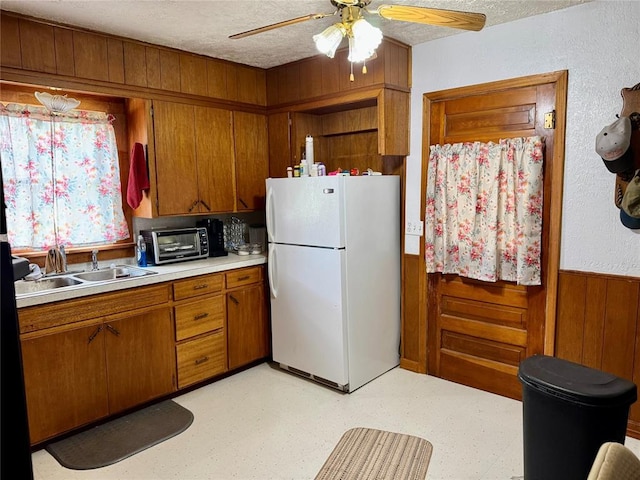 321 E Ninth St, Leedey, OK 73654 - kitchen with freestanding refrigerator, a sink, brown cabinetry, a wainscoted wall, and light countertops