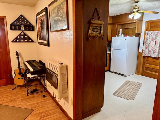 321 E Ninth St, Leedey, OK 73654 - kitchen featuring freestanding refrigerator, heating unit, ceiling fan, light wood finished floors, and wooden walls