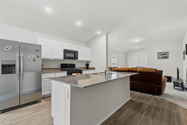 kitchen with black appliances, a sink, vaulted ceiling, light wood finished floors, and open floor plan