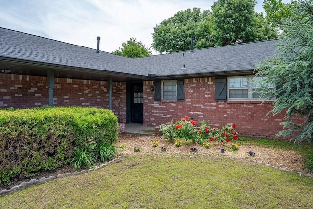 view of front of house with brick siding, a front yard, and roof with shingles