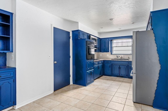 kitchen featuring freestanding refrigerator, a sink, blue cabinetry, light tile patterned floors, and decorative backsplash