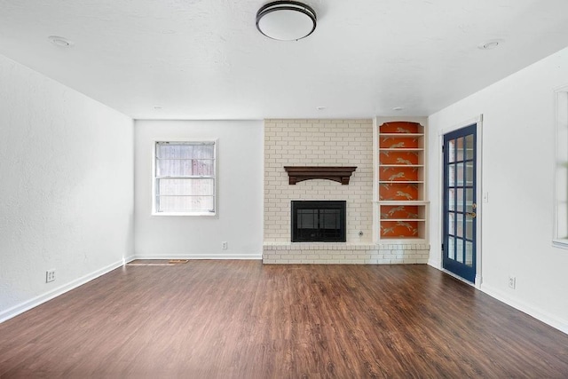 unfurnished living room with built in shelves, wood finished floors, a brick fireplace, and baseboards