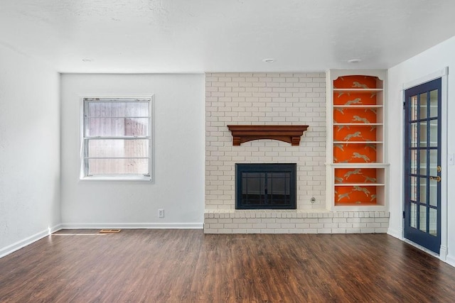 unfurnished living room featuring wood finished floors, a brick fireplace, baseboards, and built in shelves