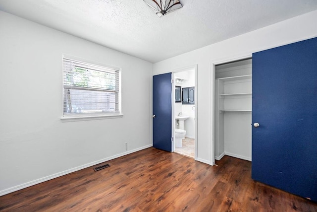 unfurnished bedroom with wood finished floors, a closet, baseboards, a textured ceiling, and connected bathroom
