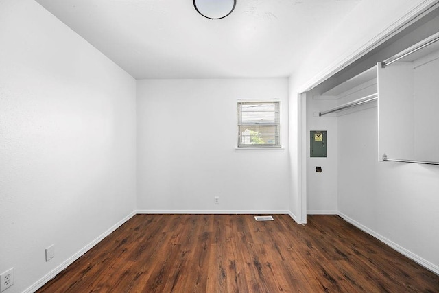 unfurnished bedroom featuring wood finished floors, baseboards, electric panel, and a closet