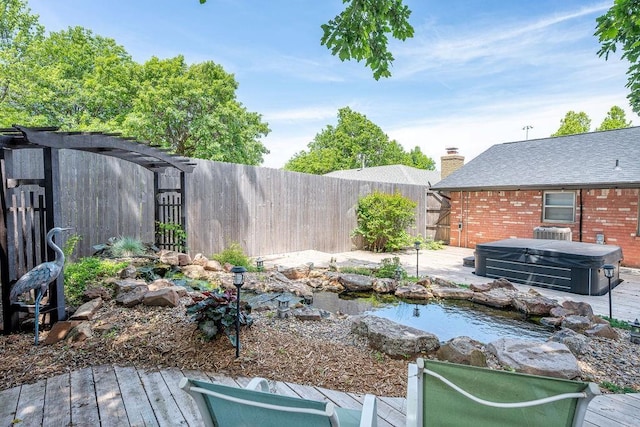 fenced backyard with a hot tub, a garden pond, central AC unit, and a deck