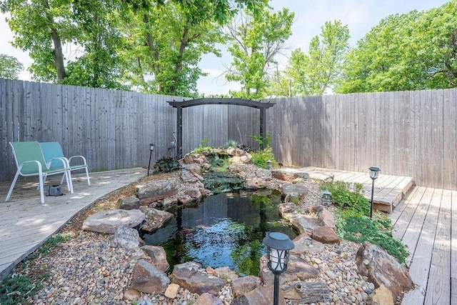 fenced backyard featuring a wooden deck and a small pond