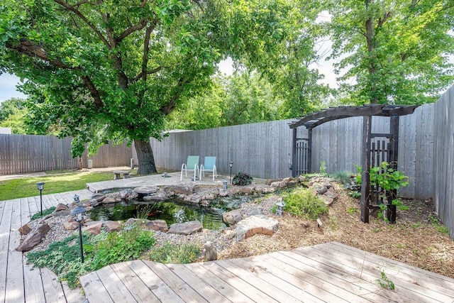 wooden terrace with a fenced backyard and a small pond