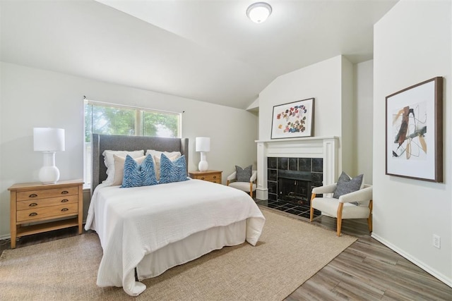 2013 Cedar Meadow Ln, Edmond, OK 73003 - bedroom featuring wood finished floors, lofted ceiling, a tiled fireplace, and baseboards